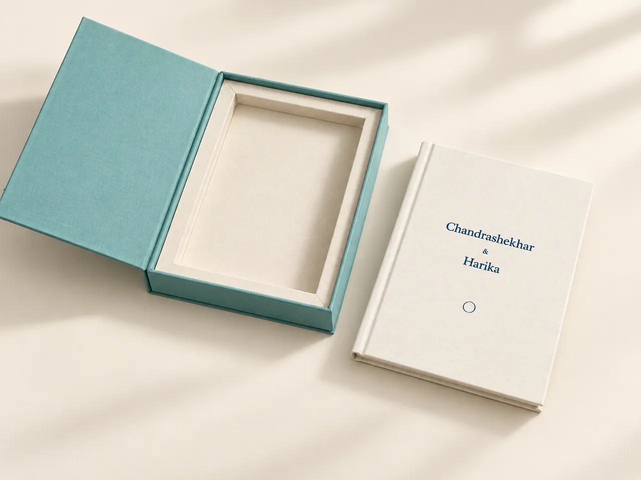 An open teal presentation box beside a cream Vowbook with a couple’s names on the cover